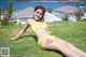 A woman in a yellow bikini laying on the grass.