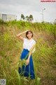 A woman in a white shirt and blue skirt standing in tall grass.