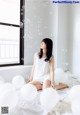 A woman sitting on a bed surrounded by white balloons.