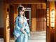 A woman in a blue kimono standing in front of a doorway.